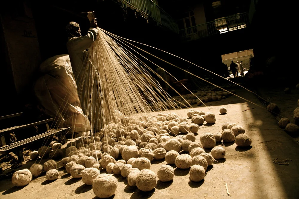 Un uomo sta facendo una matassa di fibre di lana in un mercato locale - Fotografia Fineart di Rada Akbar