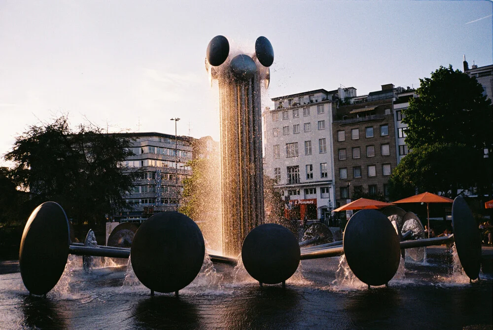 Fotokunst von Ben Hammer: ruhige Aufnahme des Ebertplatzes in Köln mit Wasserbrunnen.