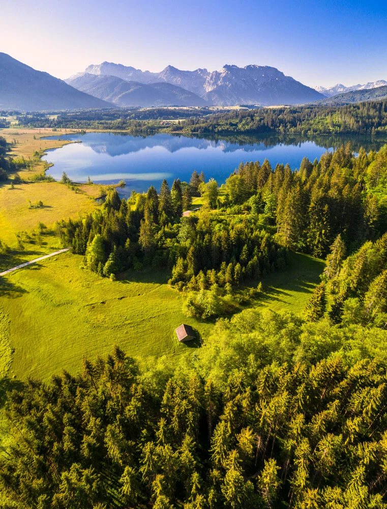 Luftaufnahme eines ruhigen Sees in Bayern, umgeben von grünen Hügeln und Bergen.