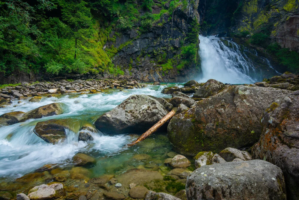 Wasserfall in den Alpen: sanft fließendes Wasser zwischen grünen Felsen.