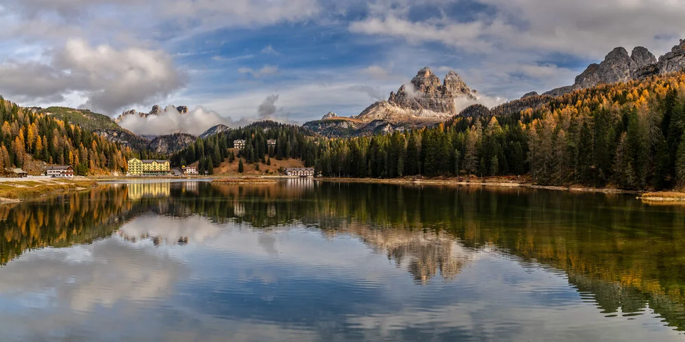 Beautiful lake in the Dolomites, surrounded by larch trees and fog.