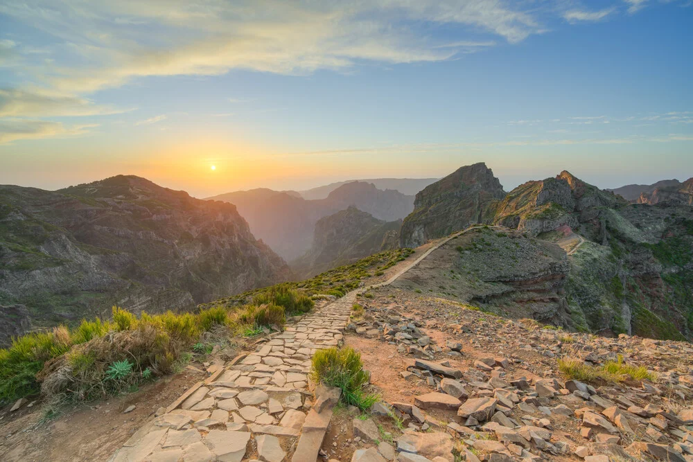 Sunset over Madeira's mountains with soft colors and rocks in the foreground.