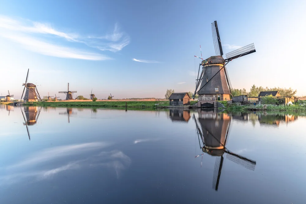 Photo of windmills in Holland, gentle water reflections and clear blue sky.