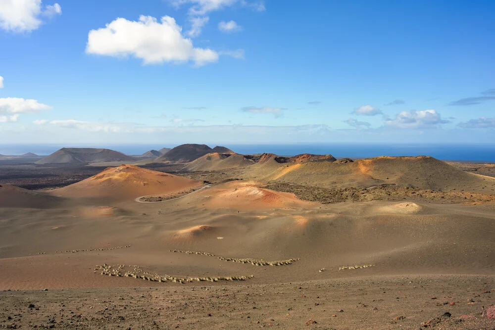 View of Timanfaya National Park with gentle volcanic landscapes and clouds in the sky.