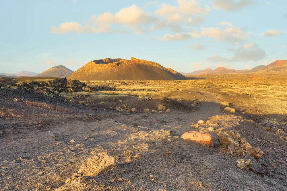 Path to El Cuervo volcano on Lanzarote with rugged terrain and soft clouds
