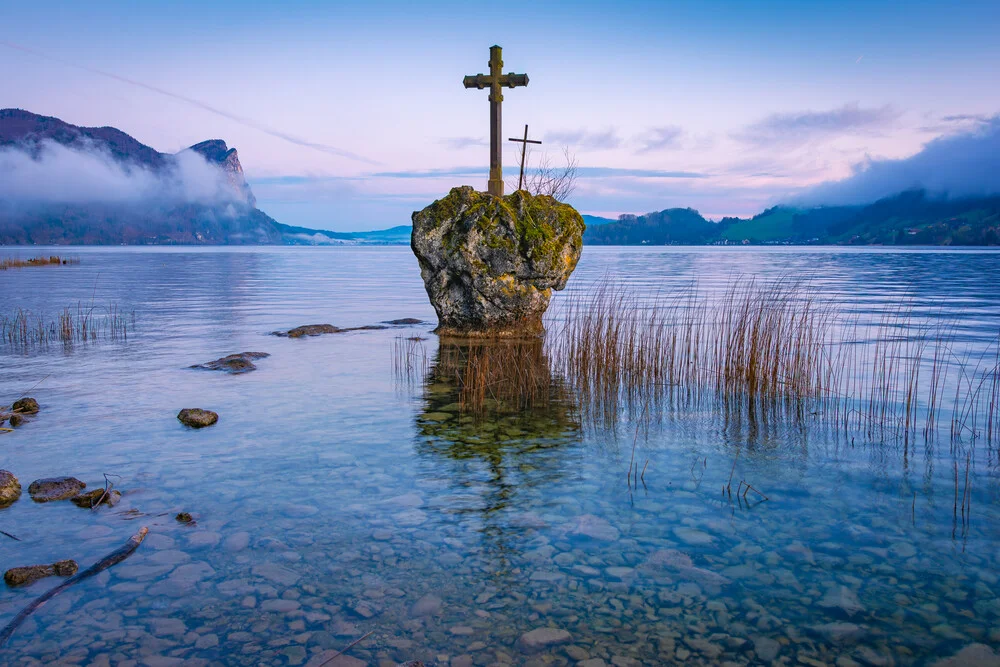 Morgendämmerung über dem Mondsee mit sanftem Nebel und Bergen im Hintergrund.