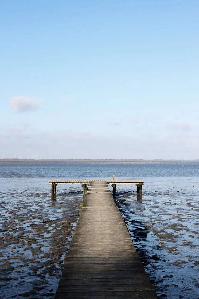Wadden Sea at low tide with a calm wooden pier near the beach.