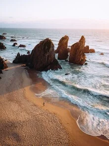 Wandbild mit einem einsamen Spaziergänger am felsigen Strand in Portugal