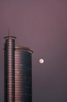 Photo art by AJ Schokora: full moon over an urban skyline in soft colors.