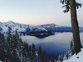 Snow-covered Crater Lake surrounded by pine trees, calm winter landscape