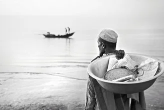 Merchant waiting by a fishing boat, holding fish in a bowl.