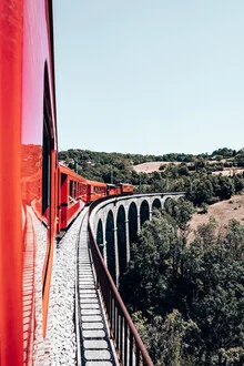 Photo art by Eva Stadler: little red train crossing a bridge in the landscape
