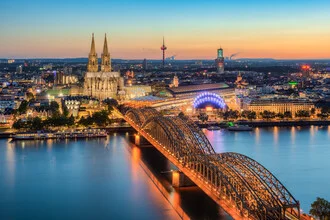View over Cologne in the evening, featuring illuminated buildings and a calm Rhine river.