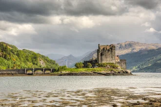Blick auf Eilean Donan Castle in Schottland mit ruhigem Wasser und Bergen im Hintergrund.