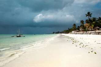 View of a boat on the white sand beach of Zanzibar under a cloudy sky.
