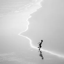Joyful boy playing on the beach with sand and water under a clear sky.