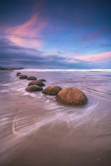 Moeraki Boulder Beach in New Zealand at sunset, calm water reflections.