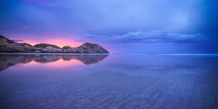 Sonnenuntergang über Wharariki Beach in Neuseeland mit reflektierenden Dünen.