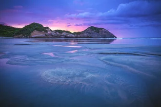 Sonnenuntergang über Wharariki Beach in Neuseeland mit sanften Dünen und ruhigem Ozean.