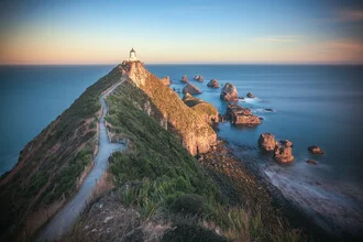 Nugget Point Lighthouse at dusk, warm light over cliffs and ocean