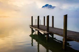 Calm lake shrouded in fog with mountains in the background at sunrise.