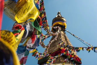 Stupa in Kathmandu adorned with colorful prayer flags under a clear sky, peaceful mood.
