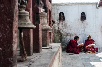 Monks sitting on the stone floor in Bodnath, Nepal, dressed in traditional clothing