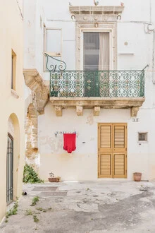 A red shirt hangs in a Mediterranean alley with white buildings.