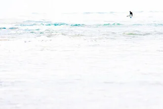 Surfer in calm water, surrounded by waves and light reflections.