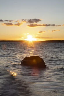 Sunset over the Baltic Sea: gentle waves and rocky shore bathed in warm light.