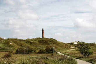 Cloudy sky above Norderney lighthouse in a peaceful landscape.