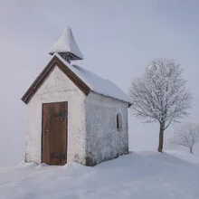 Kleine Kapelle im Schnee mit Baum in winterlicher Landschaft