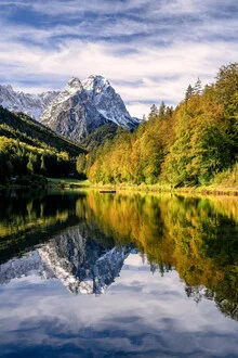 Calm autumn landscape at Lake Riessersee with colorful tree reflections.