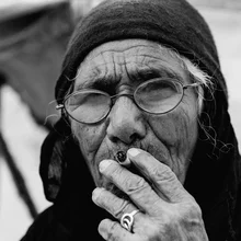 Portrait of an elderly Bedouin woman with wrinkles and glasses, relaxed and smoking in the desert.