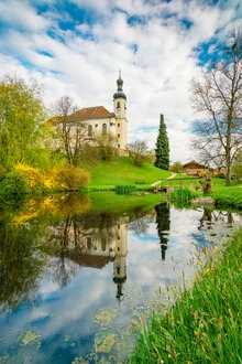 Frühling in Breitbrunn: Kirche spiegelt sich im ruhigen Chiemsee mit den Alpen im Hintergrund