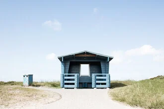 Blue house in a peaceful setting with grass and dunes, showcasing a calm summer vibe.