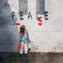 Girl with a brush and bucket writing on the wall: peace please