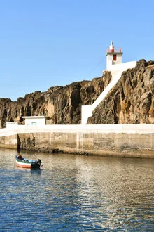 Lighthouse on the Portuguese coast: tranquil seascape with a boat and rocks in the foreground