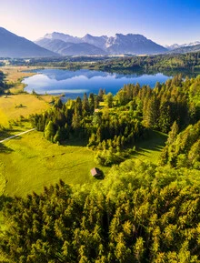 Luftaufnahme eines ruhigen Sees in Bayern, umgeben von grünen Hügeln und Bergen.