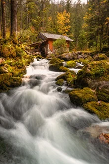 Waterfall and historic watermill in Austria surrounded by colorful autumn leaves.