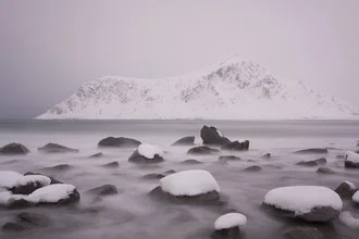 Winter landscape with snow-covered stones and calm sea in Norway