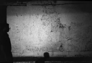 Mann in der Nacht: Silhouette vor einer hellen Wand, sanfte Licht- und Schattenspiele.