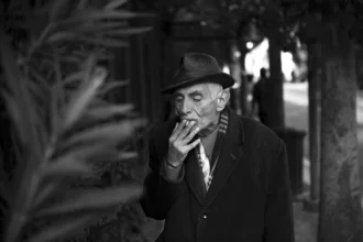 Portrait of an elderly man in formal attire, smoking and looking contemplative.