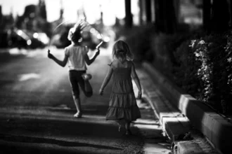 Two girls joyfully playing on the street in Athens, surrounded by warm light and shadows.
