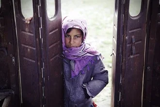 Girl stands outside a ruined bus in Afghanistan