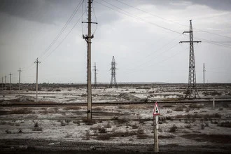 Grey desert in Uzbekistan featuring power poles and gentle hills.