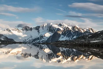 Calm mountain lake reflecting peaks in the water, surrounded by nature.