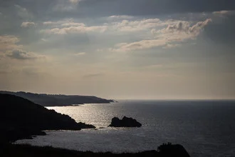 Wunderschönes Lichtspiel über der Küste in der Bretagne mit sanften Wolken und ruhigem Meer.
