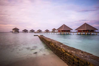 Photo art by Hannes Cmarits: serene sunrise over water bungalows