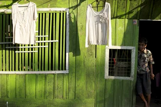 Boy in front of green house in Myanmar, calm mood with wooden structure and laundry window.